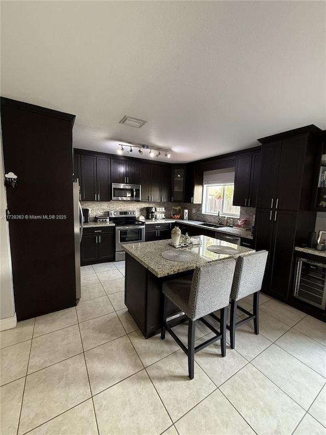 kitchen with a breakfast bar, appliances with stainless steel finishes, a center island, light stone counters, and light tile patterned flooring