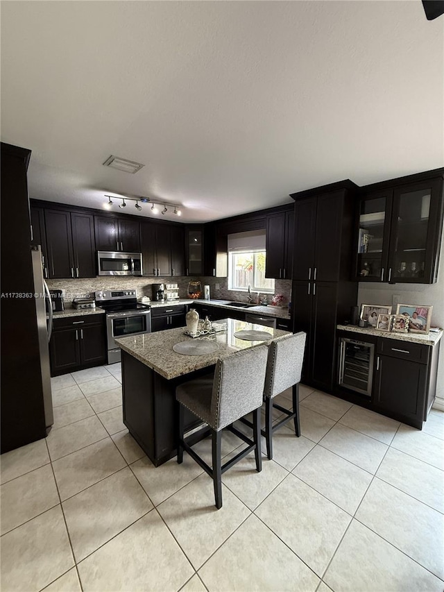 kitchen featuring a breakfast bar area, appliances with stainless steel finishes, light stone counters, wine cooler, and a kitchen island