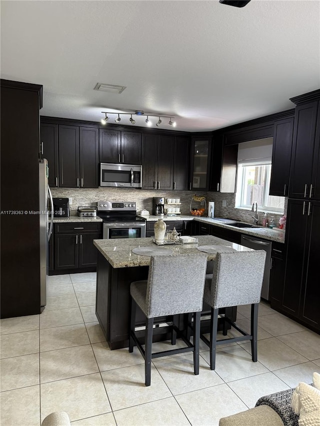 kitchen featuring a breakfast bar, sink, a center island, appliances with stainless steel finishes, and light stone countertops