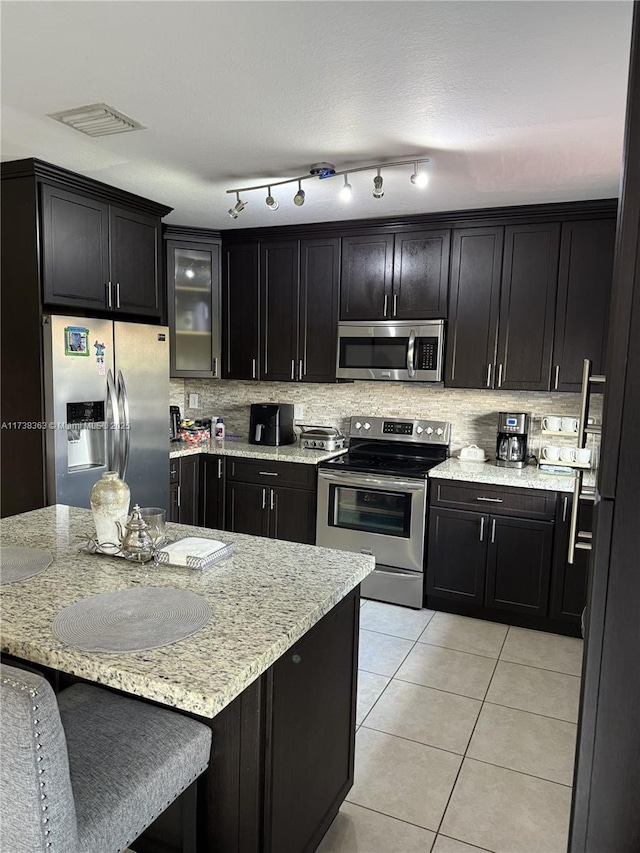 kitchen featuring a breakfast bar, light stone counters, light tile patterned floors, appliances with stainless steel finishes, and backsplash