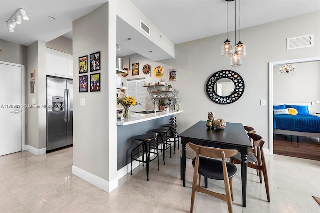 dining area with a kitchen bar, sink, kitchen peninsula, pendant lighting, and white cabinets