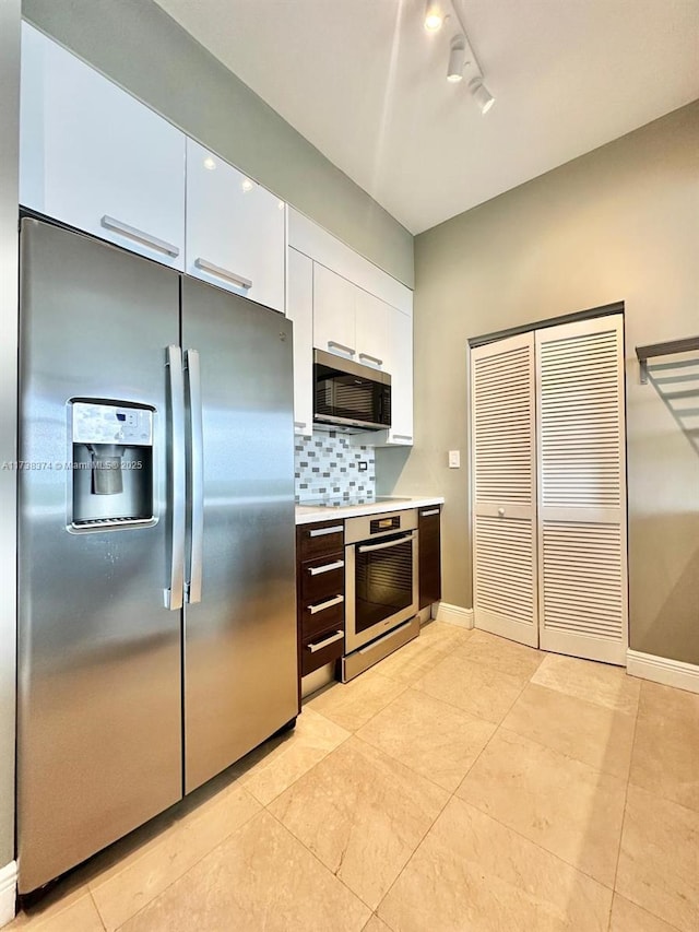 kitchen with light tile patterned floors, rail lighting, appliances with stainless steel finishes, white cabinets, and decorative backsplash