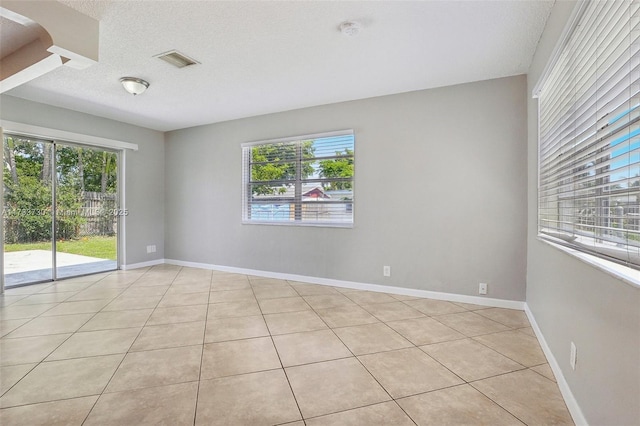 tiled spare room with a textured ceiling and a wealth of natural light