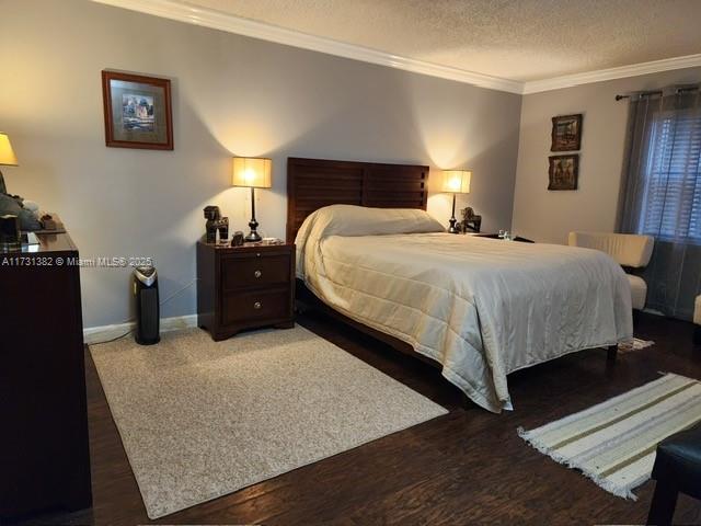 bedroom with dark wood-type flooring, ornamental molding, and a textured ceiling