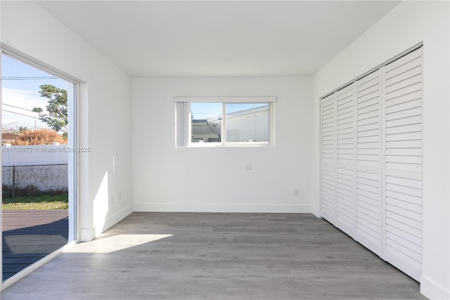 unfurnished bedroom featuring multiple windows, hardwood / wood-style flooring, access to exterior, and a closet