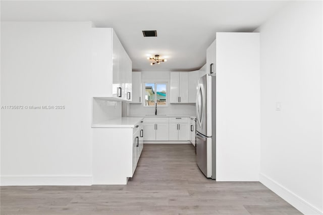 kitchen featuring sink, light hardwood / wood-style floors, stainless steel refrigerator, and white cabinets