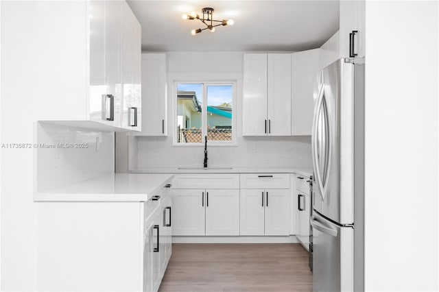 kitchen featuring stainless steel refrigerator, light wood-type flooring, sink, and white cabinets