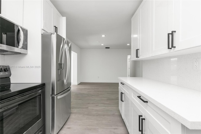 kitchen with stainless steel appliances, tasteful backsplash, white cabinets, and light hardwood / wood-style floors