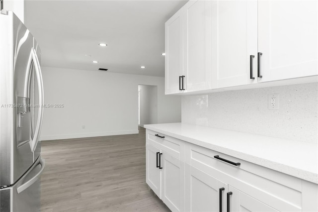 kitchen featuring white cabinetry, stainless steel fridge with ice dispenser, light hardwood / wood-style flooring, and tasteful backsplash