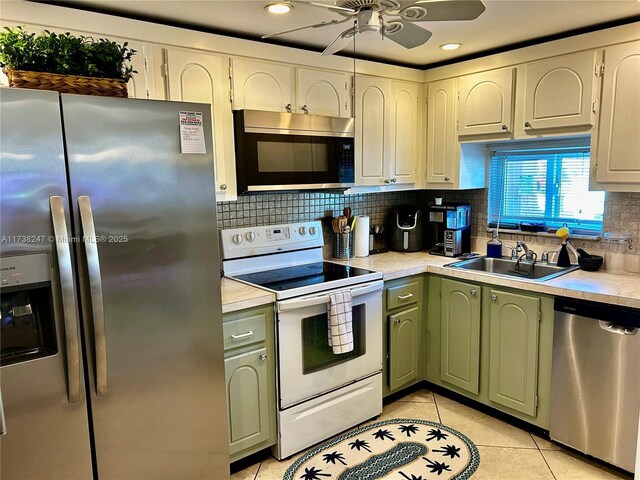 kitchen featuring appliances with stainless steel finishes, sink, decorative backsplash, light tile patterned floors, and green cabinetry