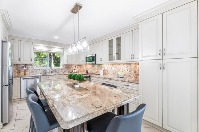 kitchen with light tile patterned flooring, appliances with stainless steel finishes, white cabinets, a kitchen bar, and a center island