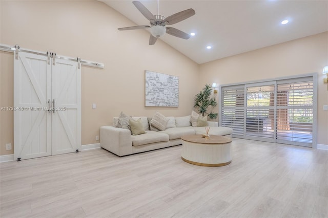 living room with ceiling fan, a barn door, high vaulted ceiling, and light wood-type flooring