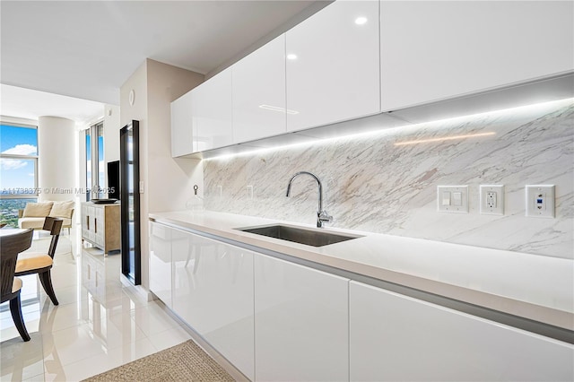 kitchen with decorative backsplash, modern cabinets, expansive windows, white cabinetry, and a sink