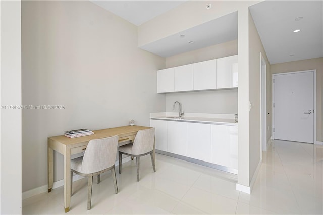 kitchen with light countertops, a sink, white cabinetry, and baseboards