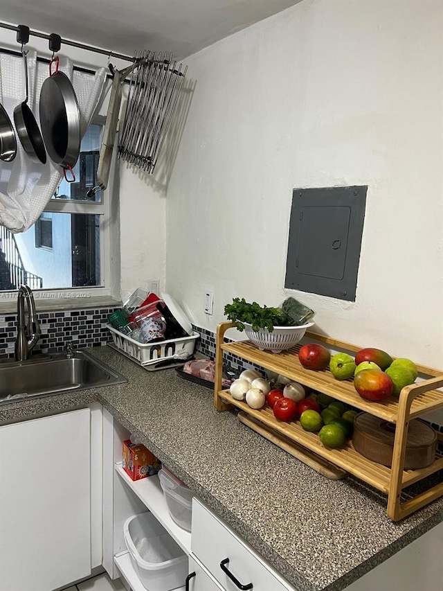 kitchen with white cabinetry, sink, electric panel, and backsplash