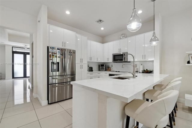 kitchen featuring decorative light fixtures, white cabinetry, a kitchen breakfast bar, kitchen peninsula, and stainless steel appliances