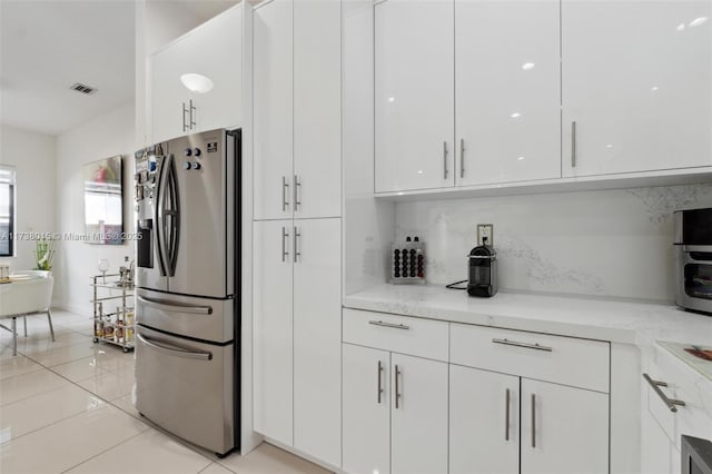 kitchen featuring white cabinetry, tasteful backsplash, light tile patterned floors, stainless steel fridge, and light stone countertops