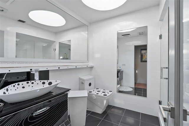 bathroom with toilet, a shower with shower door, tile walls, vanity, and tile patterned flooring