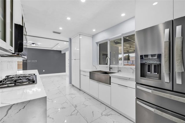 kitchen with light stone counters, appliances with stainless steel finishes, sink, and white cabinets