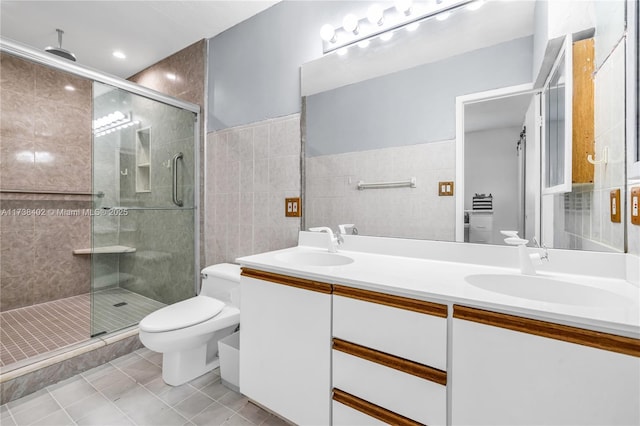 bathroom featuring toilet, tile walls, vanity, a shower with door, and tile patterned flooring