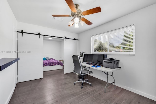 home office featuring a barn door, dark wood-type flooring, and ceiling fan