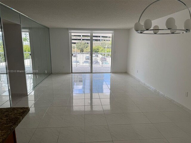 unfurnished room featuring a notable chandelier, a wealth of natural light, tile patterned floors, and a textured ceiling