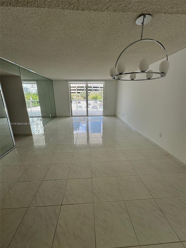 tiled empty room featuring a notable chandelier, a textured ceiling, and a healthy amount of sunlight