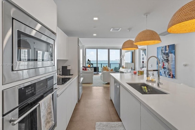 kitchen with stainless steel appliances, a water view, white cabinets, and decorative light fixtures