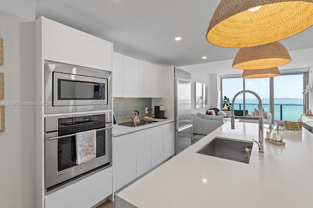 kitchen featuring sink, a water view, built in appliances, decorative light fixtures, and white cabinets