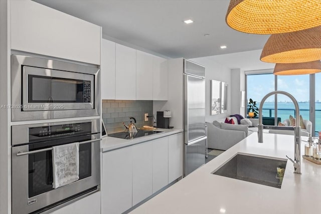 kitchen with sink, a water view, white cabinetry, built in appliances, and backsplash