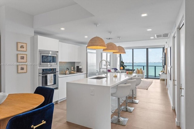 kitchen with sink, a water view, hanging light fixtures, a center island with sink, and stainless steel appliances