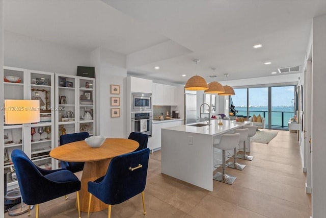 kitchen featuring pendant lighting, appliances with stainless steel finishes, a water view, an island with sink, and white cabinets