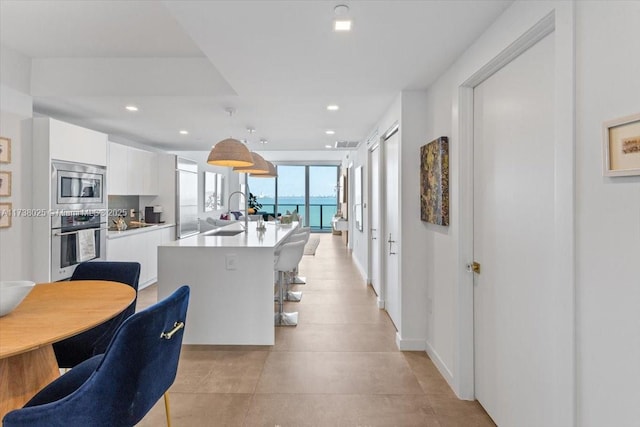 kitchen with appliances with stainless steel finishes, white cabinetry, sink, hanging light fixtures, and a center island with sink