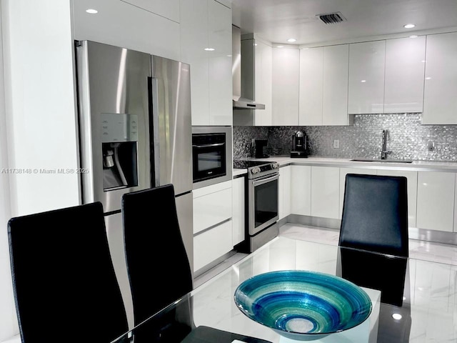 kitchen featuring white cabinetry, appliances with stainless steel finishes, sink, and wall chimney range hood