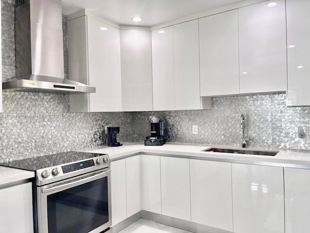 kitchen with electric stove, white cabinets, sink, and wall chimney exhaust hood