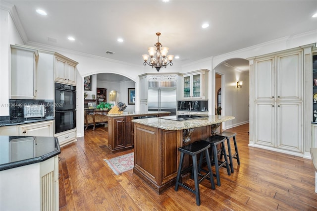 kitchen featuring hanging light fixtures, wood-type flooring, black appliances, a kitchen island, and dark stone counters