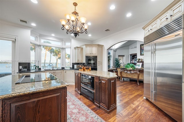 kitchen featuring light stone counters, decorative light fixtures, black appliances, and a center island