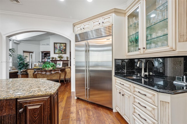 kitchen featuring cream cabinets, crown molding, dark stone counters, and built in refrigerator