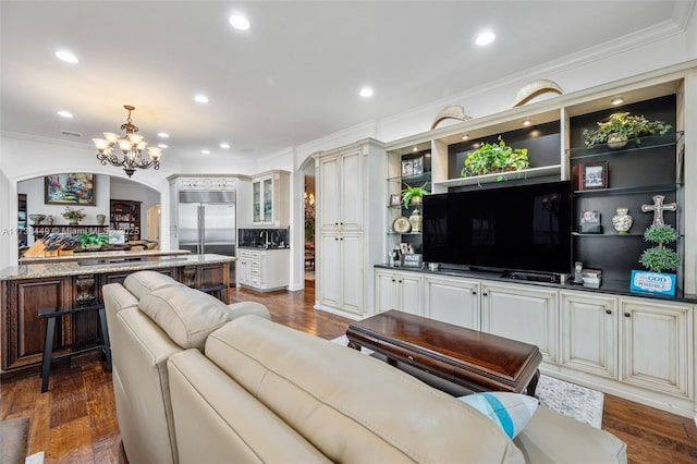 living room with an inviting chandelier, dark wood-type flooring, and ornamental molding