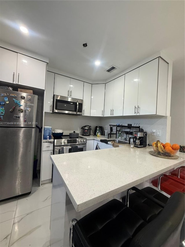 kitchen with sink, a breakfast bar area, stainless steel appliances, white cabinets, and kitchen peninsula