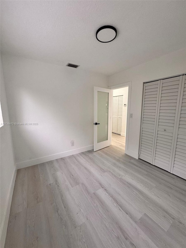 unfurnished bedroom with a textured ceiling, light wood-type flooring, and a closet