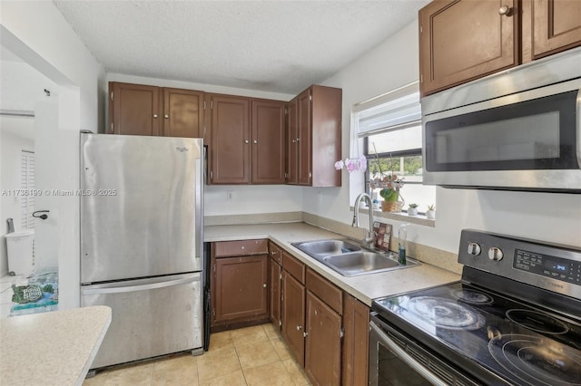 kitchen with stainless steel appliances, sink, light tile patterned floors, and a textured ceiling