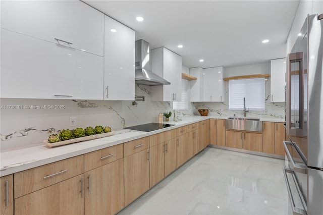 kitchen with wall chimney exhaust hood, white cabinetry, light brown cabinets, stainless steel refrigerator, and black electric cooktop