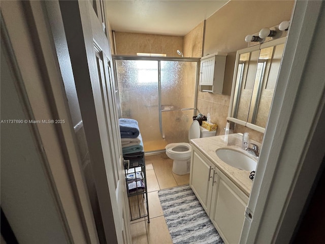 bathroom with tile walls, toilet, a shower stall, vanity, and tile patterned flooring