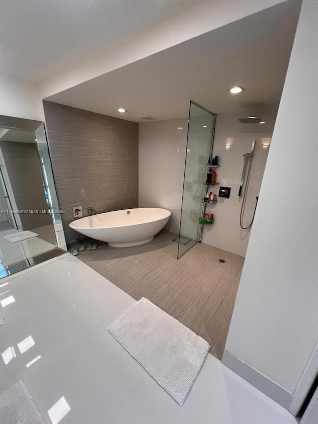 bathroom with shower with separate bathtub and tile walls