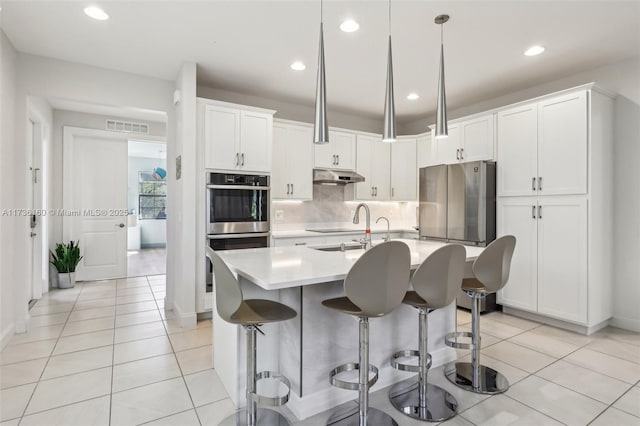 kitchen with hanging light fixtures, light tile patterned flooring, a center island with sink, and white cabinets