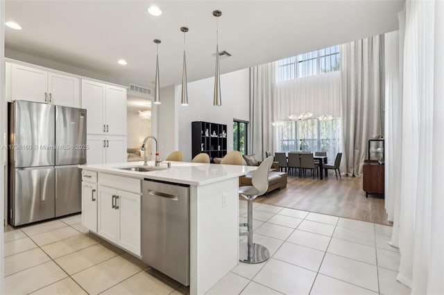 kitchen featuring light tile patterned floors, appliances with stainless steel finishes, an island with sink, pendant lighting, and white cabinets