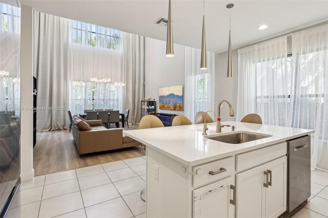 kitchen featuring light tile patterned flooring, sink, white cabinetry, decorative light fixtures, and an island with sink