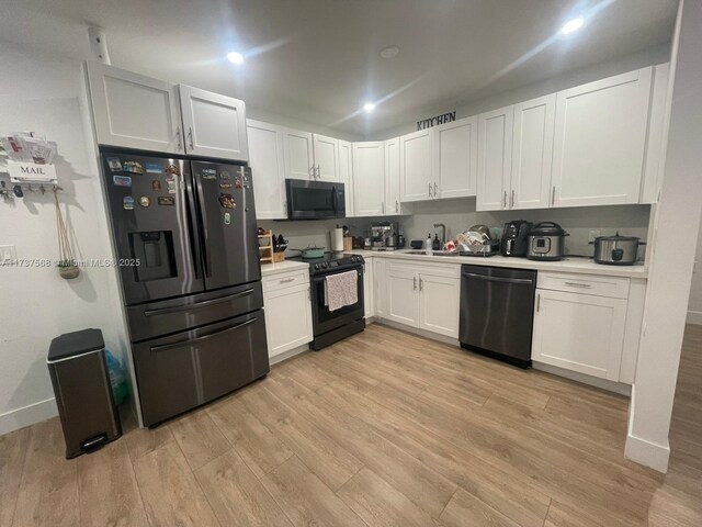 kitchen featuring white cabinetry, sink, light hardwood / wood-style floors, and black appliances