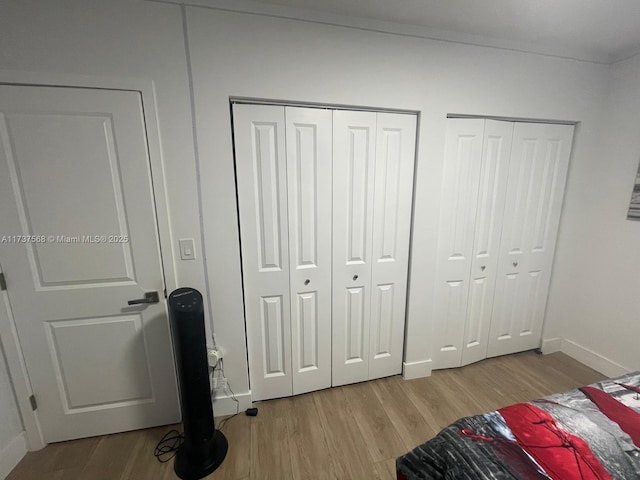 bedroom with light hardwood / wood-style floors and multiple closets